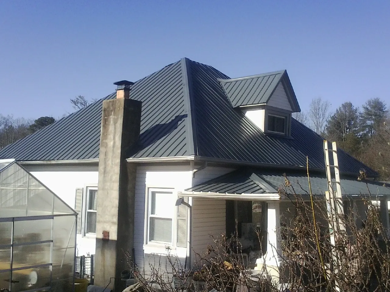 Dark blue standing seam metal roof on a white farmhouse with dormer — Slate & Tile Roof Repair by Roofing Brothers in Poynette