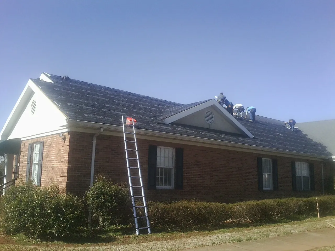 Crew tearing shingles off a brick ranch roof with a ladder set — Emergency Roof Repair work by our crew in Poynette