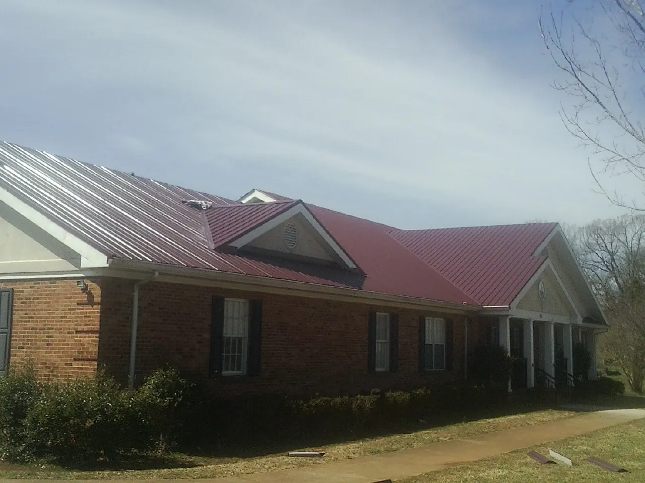 Red metal roof with gabled entries on a long brick building, from a Hail Damage Roof Repair job in Poynette