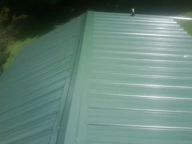 New green metal panels meeting at the ridge of a roof — Flat Roof Repair work by our crew in Poynette