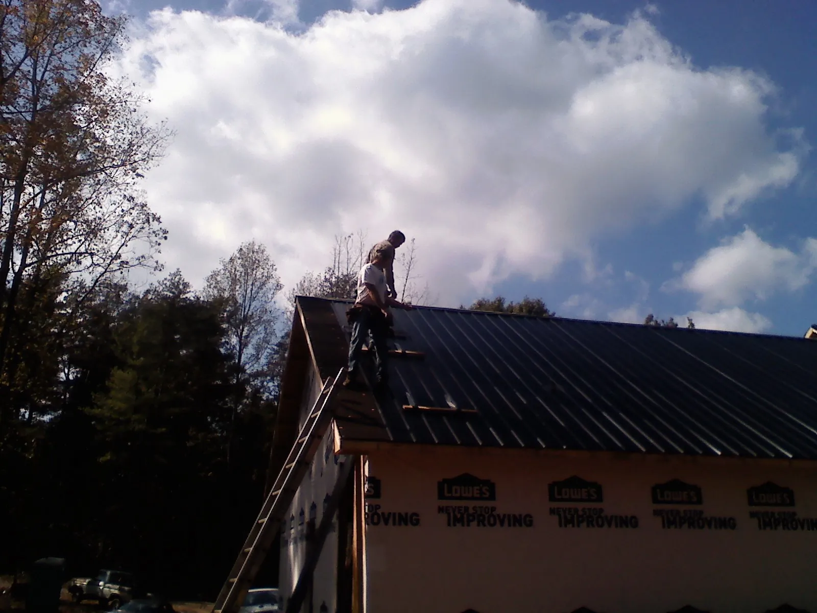 Roofer fastening dark metal panels high against a cloudy sky, from a Roof Inspection job in Poynette