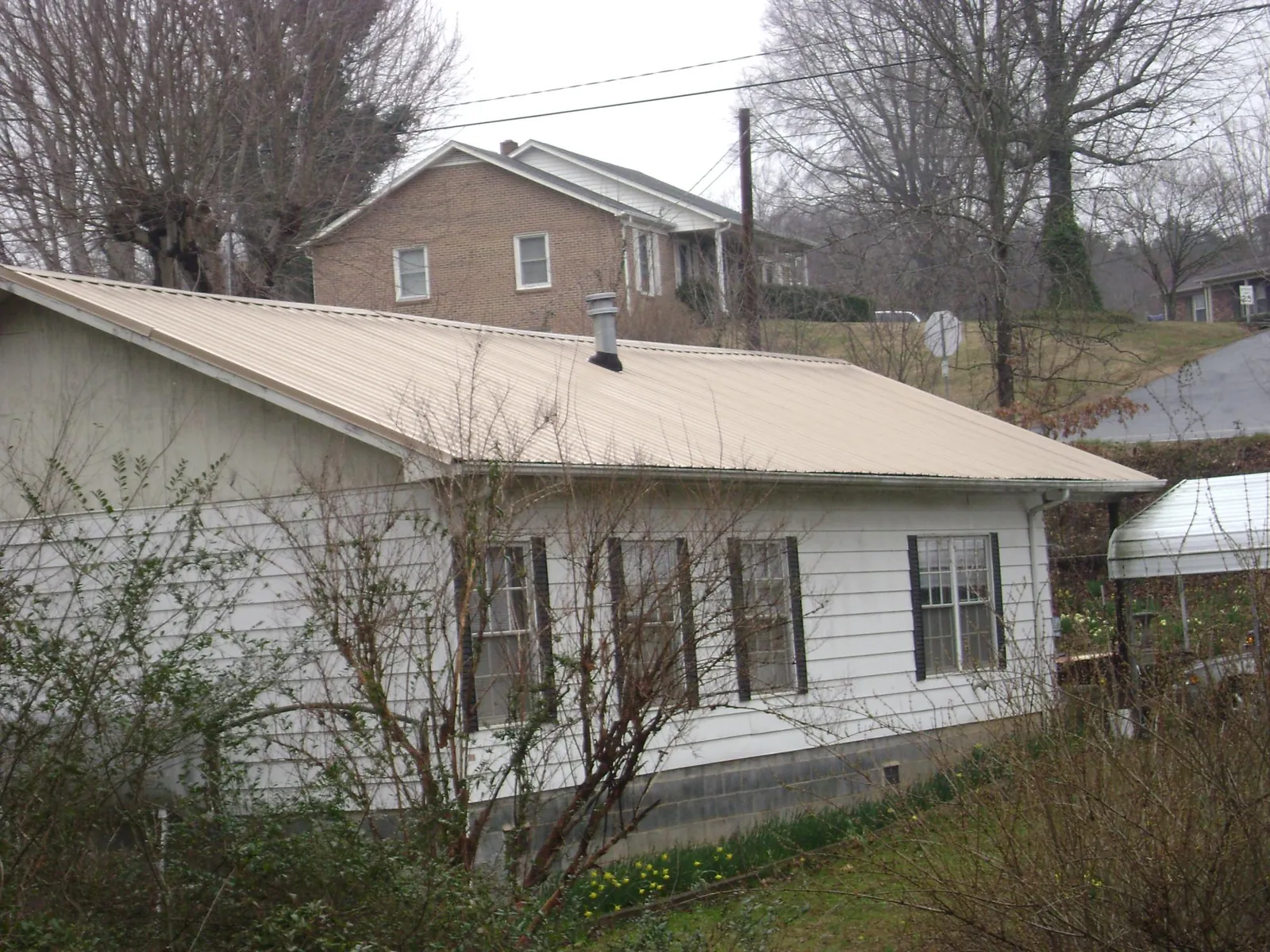 Tan metal roof on a white sided house set into a hillside — Commercial Roofing by Roofing Brothers in Poynette